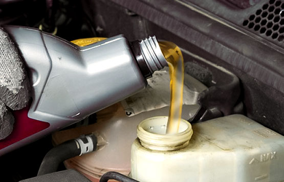 Mano con guante sirviendo una botella de líquido de frenos en el tanque